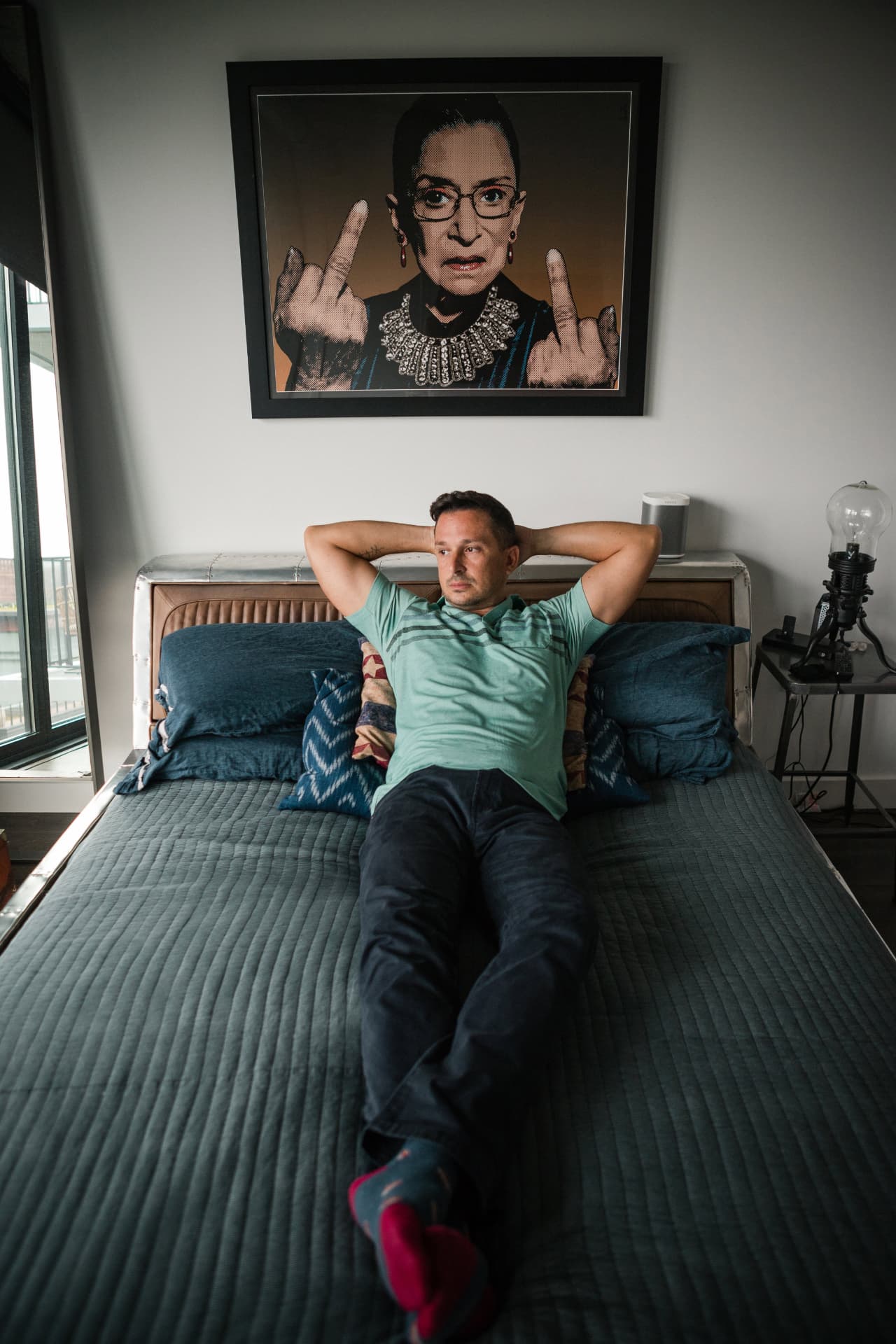 Man relaxing on a bed beneath a framed portrait